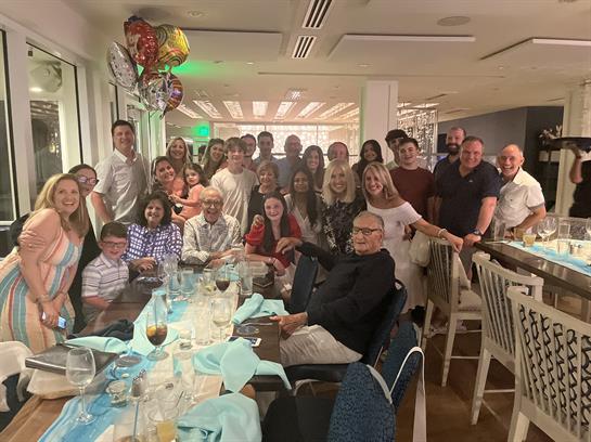 Group of family and friends celebrate together at a restaurant, enjoying food and balloons.