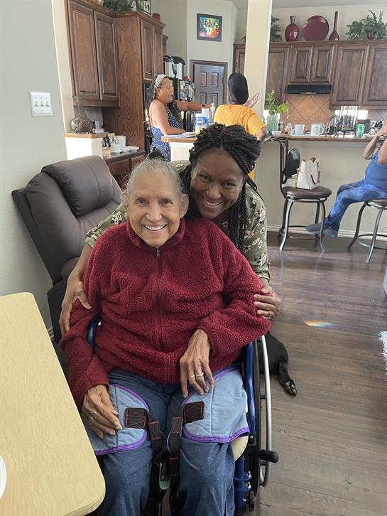 A woman sitting on a wheelchair with her arm around another woman