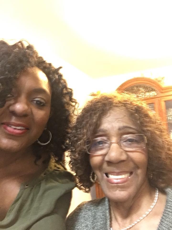 Two women are smiling happily while standing closely in a warm and inviting indoor space.