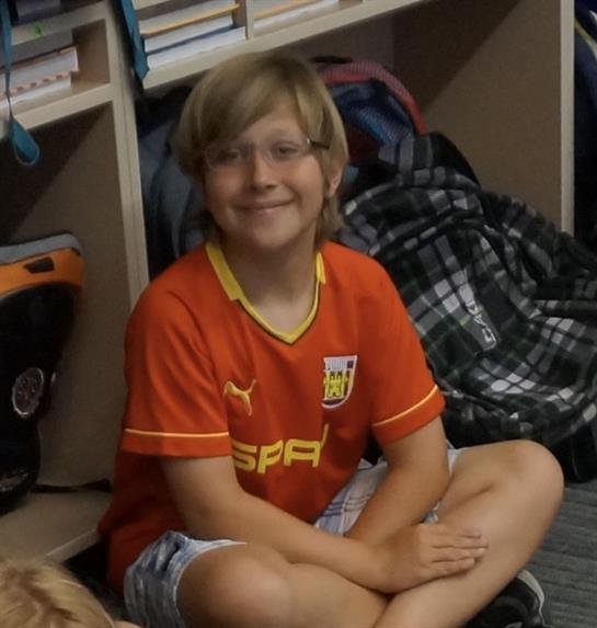 A young boy sits cross-legged on the floor, smiling happily in a cozy room filled with bags.