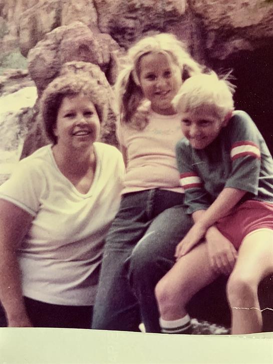 Three family members share smiles while sitting on a rock, enjoying a sunny afternoon together.