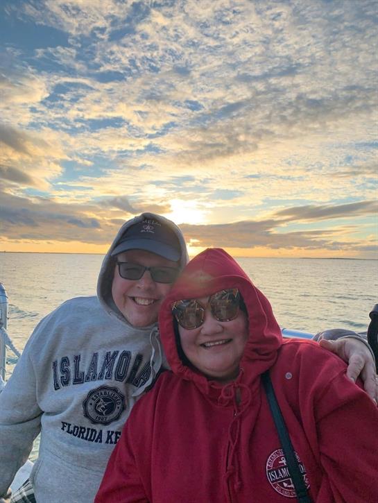 Two friends smile for a photo during a boat ride as the sun sets over the water.