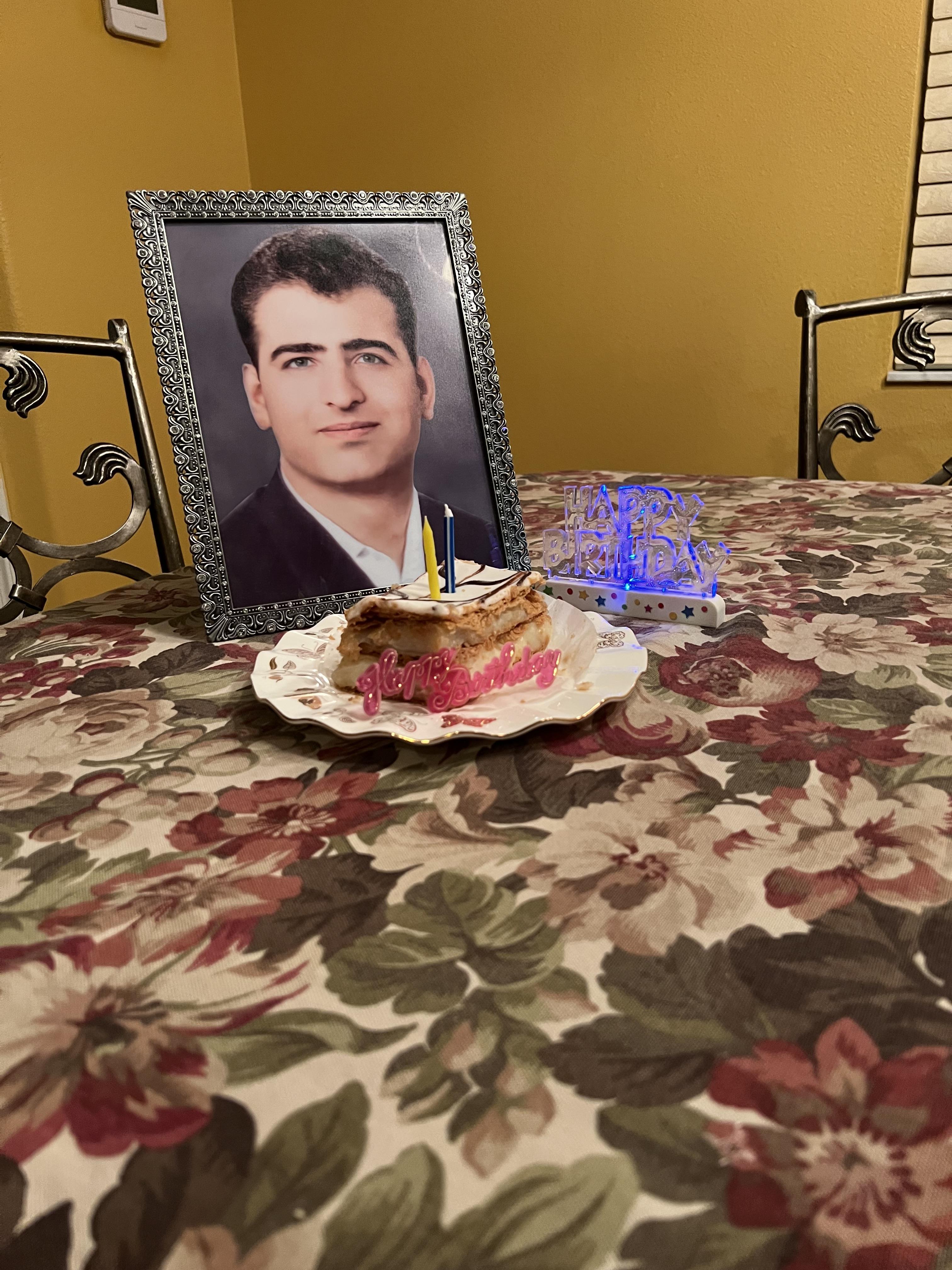 A family gathers around a table decorated with flowers, celebrating with cake and a portrait.