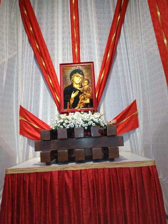 A religious artwork is prominently featured on a decorated altar with red drapes and flowers.