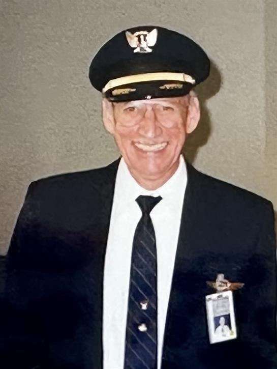 A cheerful senior pilot stands in a professional uniform, working at an airport terminal.