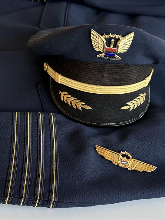Close-up view of a pilot's cap, jacket with stripes, and wings insignia displayed together.