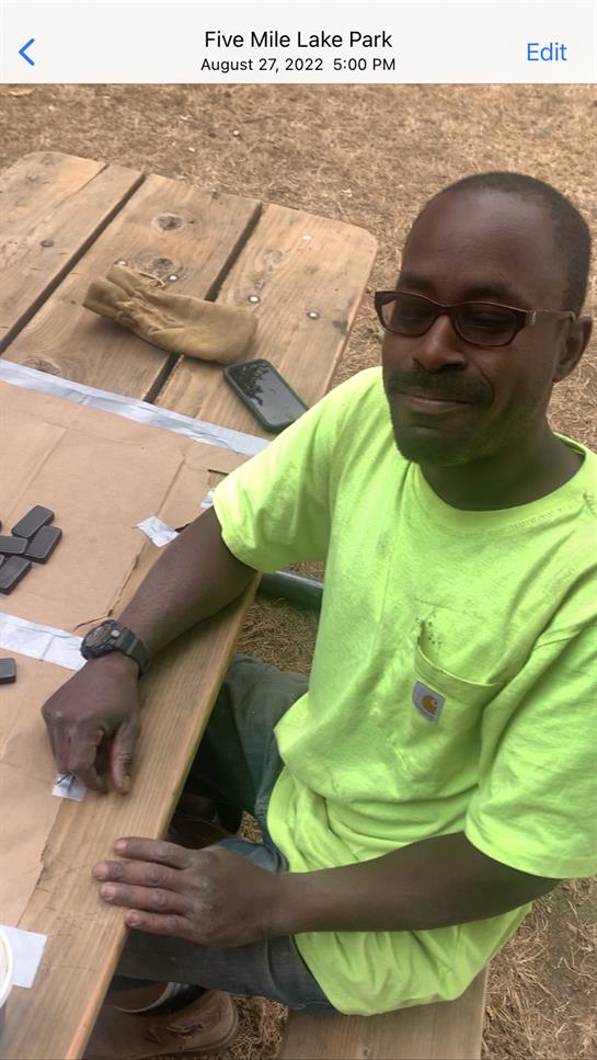 A man sits at a wooden table while organizing tools, wearing a bright green shirt and glasses.