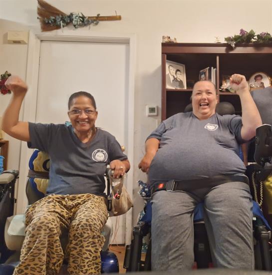 Two women engage in a joyful moment in a cozy indoor space, smiling and cheering together.