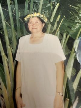 A woman stands among tall green plants wearing a floral crown at a festive outdoor event.