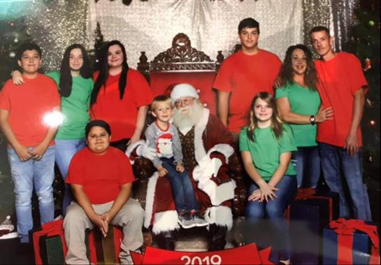 A lively group of children and adults poses with Santa Claus, dressed in holiday colors.