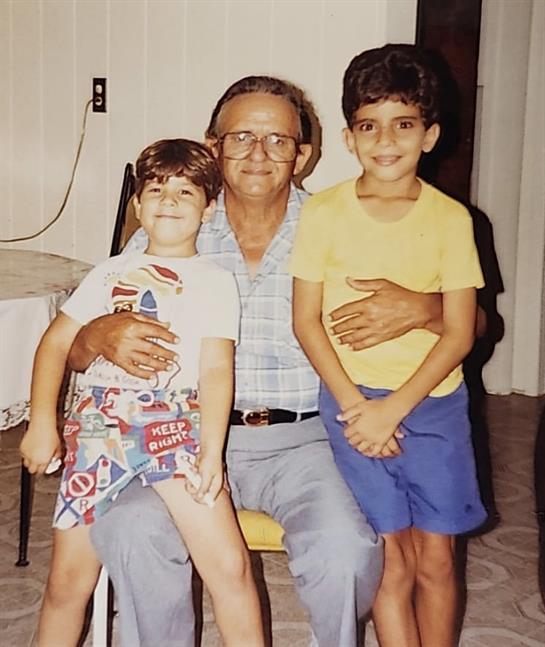 Two boys pose happily with their grandfather, showcasing a warm family bond in a simple room.