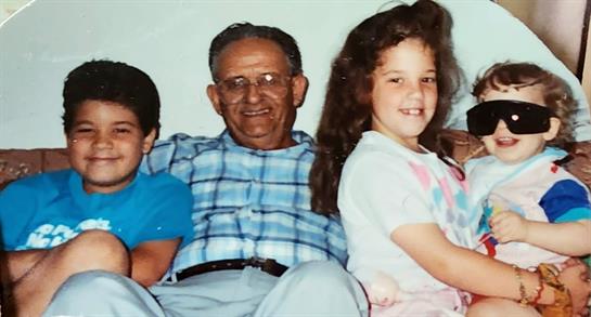 Grandfather enjoys quality time with two kids, smiling and sitting comfortably at home.