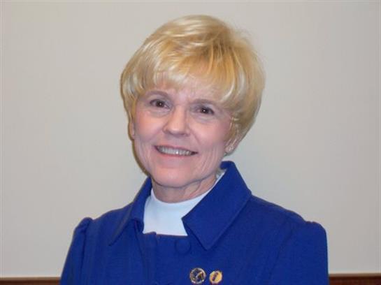 A woman with short blonde hair is smiling and wearing a blue outfit during a professional gathering.