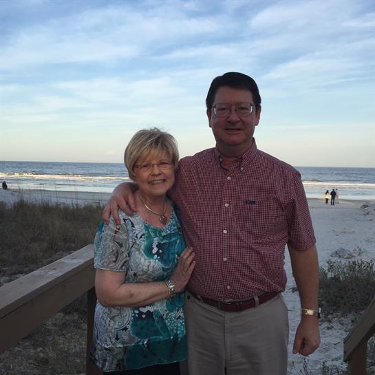 Couple stands together on a boardwalk overlooking the beach at dusk, radiating joy and love.