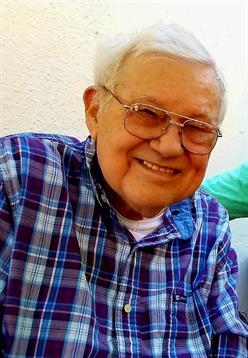 An elderly man with glasses smiles happily with friends indoors, spreading joy.