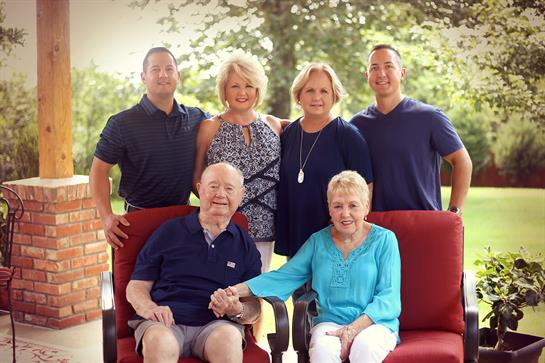 A cheerful family gathers outdoors, smiling and enjoying each other's company on a sunny day.