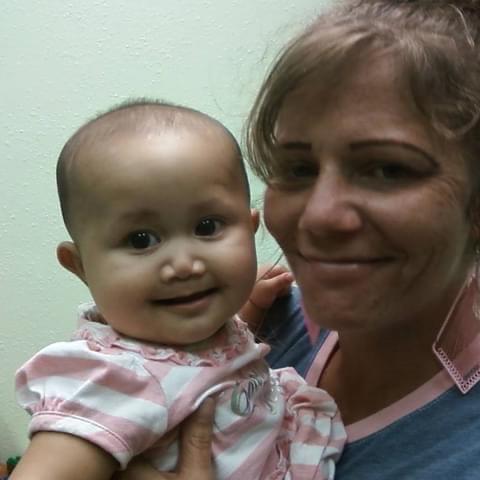 Mother and baby share a warm moment, both smiling happily in a comfortable indoor space.