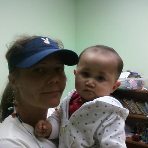 A woman lovingly holds her baby in a bright room with green walls, creating a warm atmosphere.