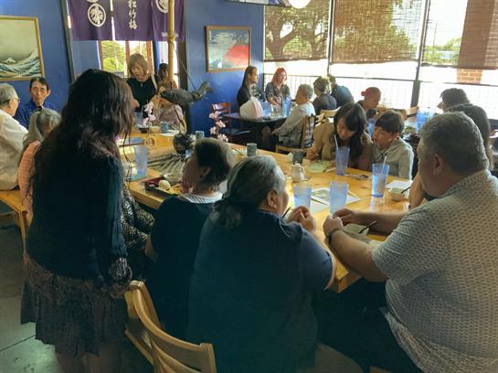 Friends and families are gathered around a large table, sharing food and laughter in a cozy space.