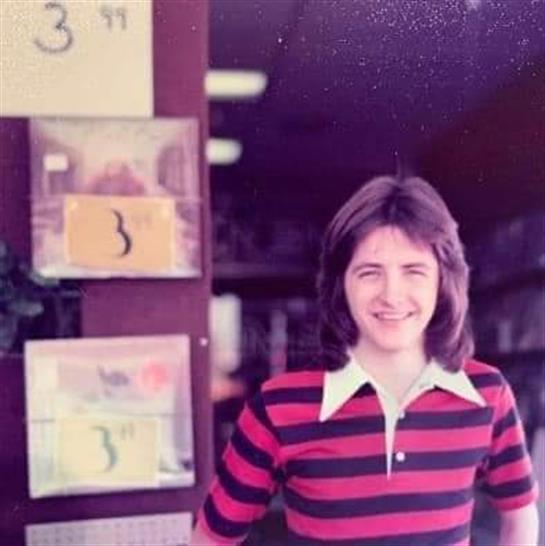 A cheerful student poses outside a classroom surrounded by colorful bulletin board displays.