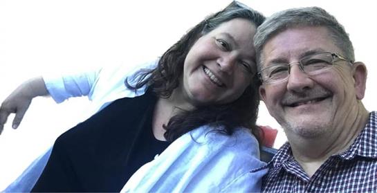 Smiling couple enjoys each other's company in a park under clear skies and warm sunshine.