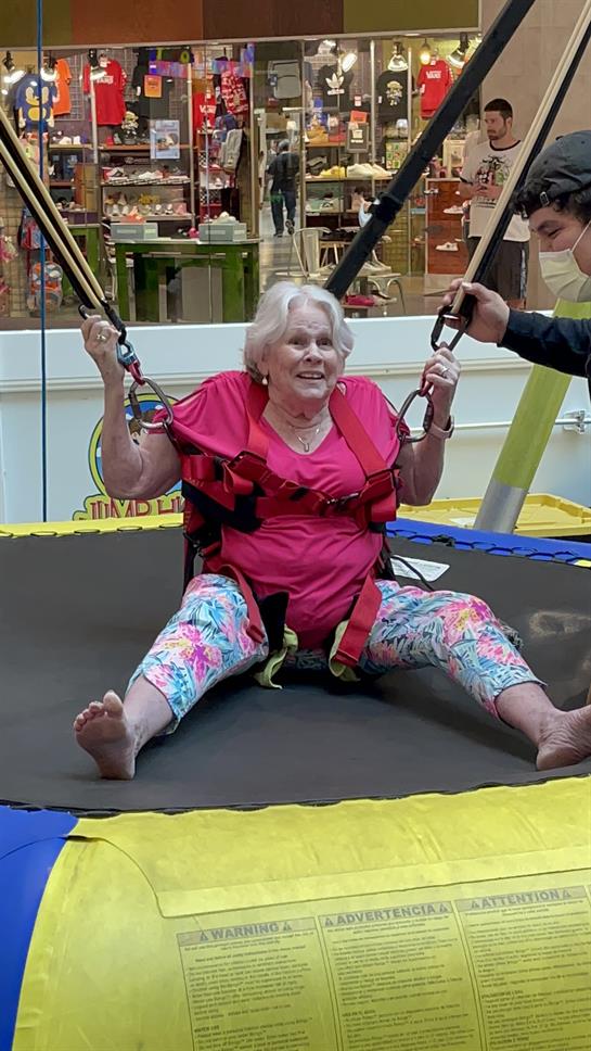 Excited elderly woman experiences trampoline bounce with a harness while smiling widely.