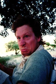 A man makes a humorous expression outdoors under a tree, enjoying the surroundings.