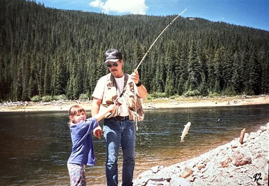 A boy excitedly shows off his catch while fishing with his father at a beautiful lakeside.