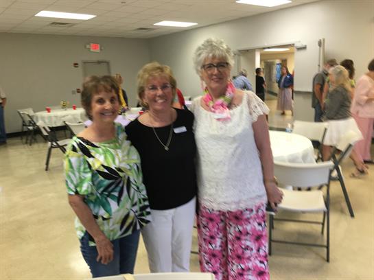 Three women pose together at a community center, enjoying a lively summer gathering with friends.