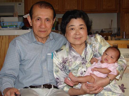 An elderly couple enjoy a special moment as they hold their newborn grandchild in a warm kitchen.