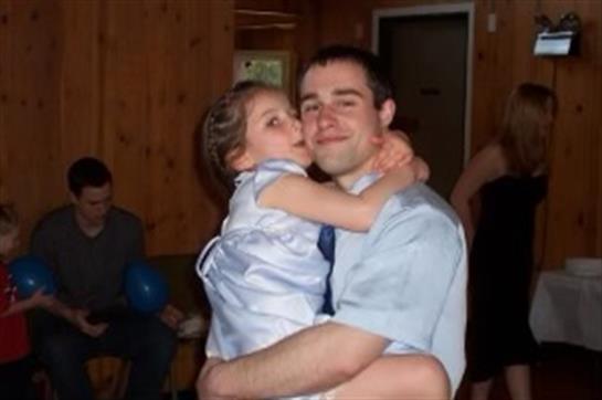 A father embraces his daughter, who is happily kissing his cheek during a family gathering.
