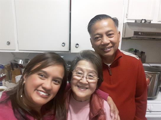 Three family members share smiles and warmth in a home kitchen setting.