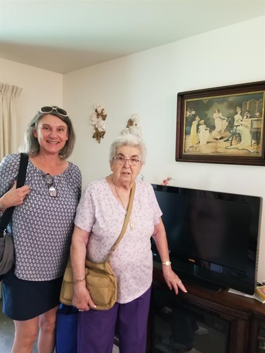 Two women stand side by side in a warm living room, smiling while enjoying their time together.