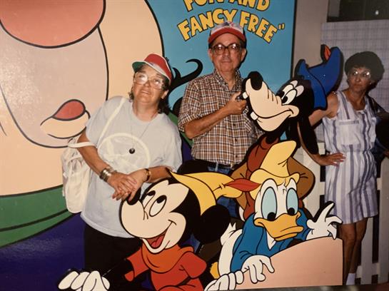 Happy couple poses in front of colorful cartoon characters at a theme park.