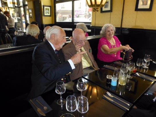 Three elderly friends engage in cheerful conversation while dining at a restaurant.