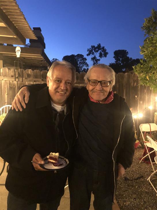 Two friends smile, holding a plate of cake at an evening gathering.