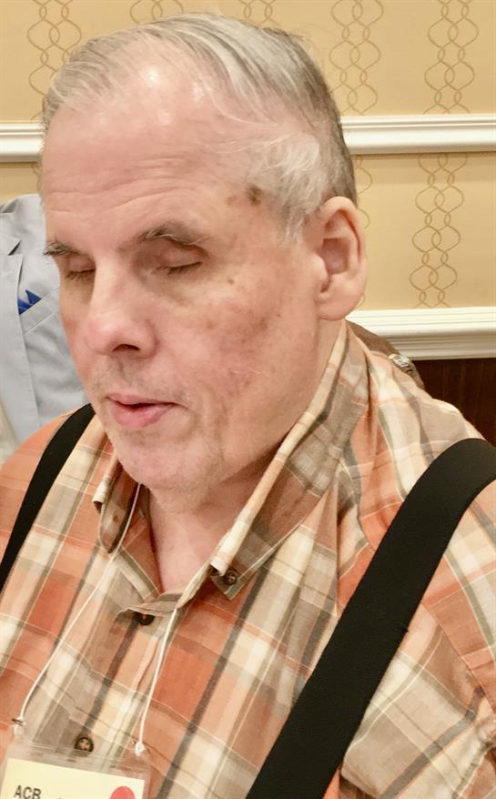 An elderly man sits quietly, eyes closed, deep in thought at a community center event.