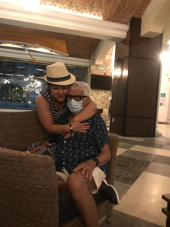 A woman and an elderly man embrace happily in a stylish lounge area with soft lighting.