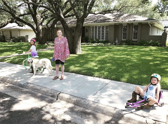 Two children enjoy a sunny day riding bicycles while a dog stands nearby in a grassy area.