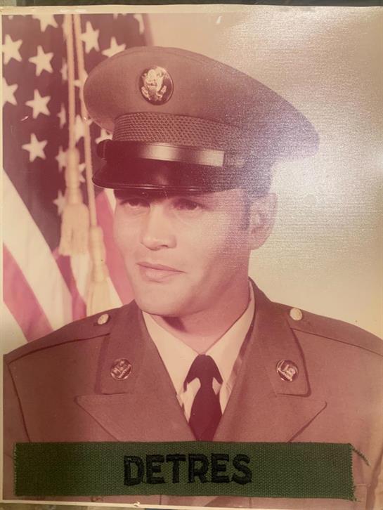 A man in a military uniform stands proudly in front of an American flag, showcasing his service.