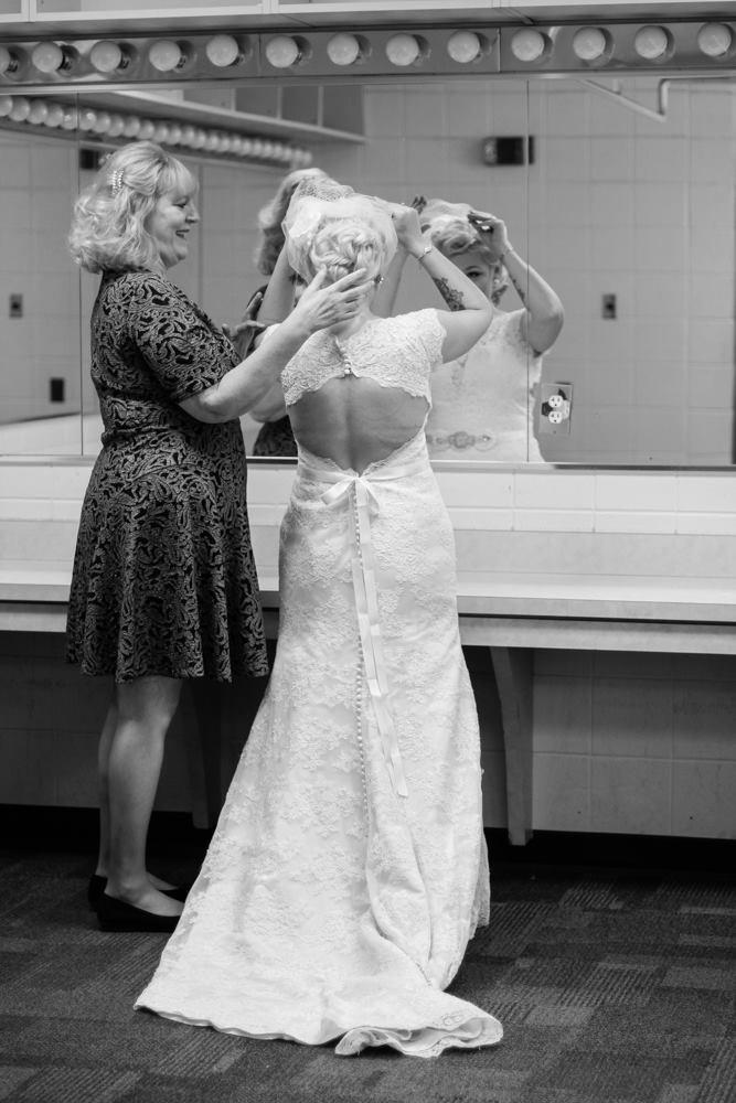 A woman adjusts another woman’s hair while she wears an elegant wedding dress in a dressing area.