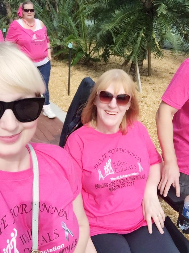 Three friends smile while sitting together at a sunny outdoor gathering, wearing matching shirts.