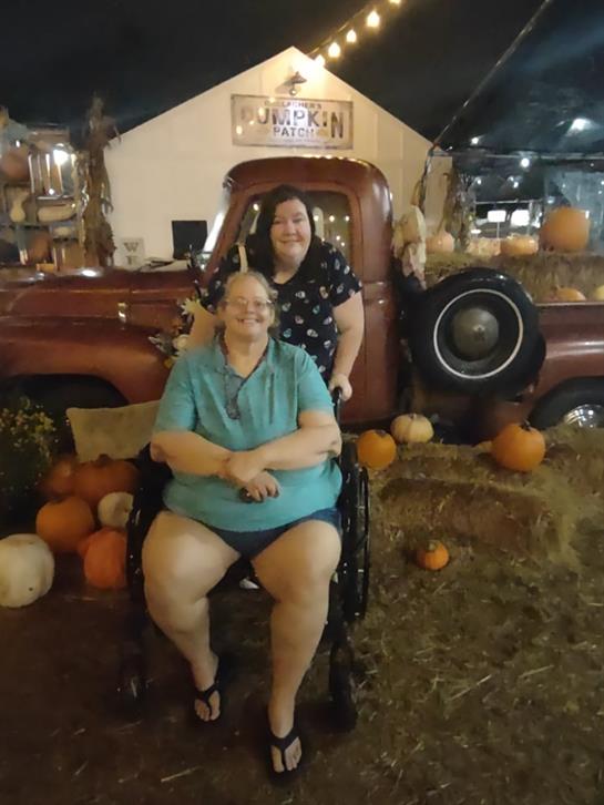 Two friends are celebrating fall next to a vintage truck surrounded by pumpkins and autumn decor.