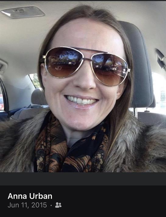 A woman is seated in a car, smiling while wearing sunglasses and a stylish scarf.