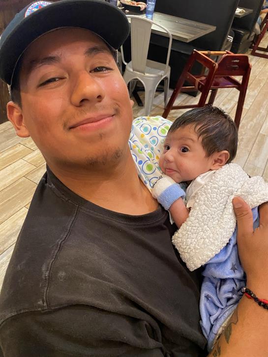 A man joyfully cuddles a baby, both beaming with happiness in a lively restaurant environment.