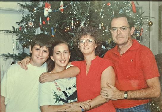 A family poses happily beside a Christmas tree adorned with ornaments in a cozy home setting.