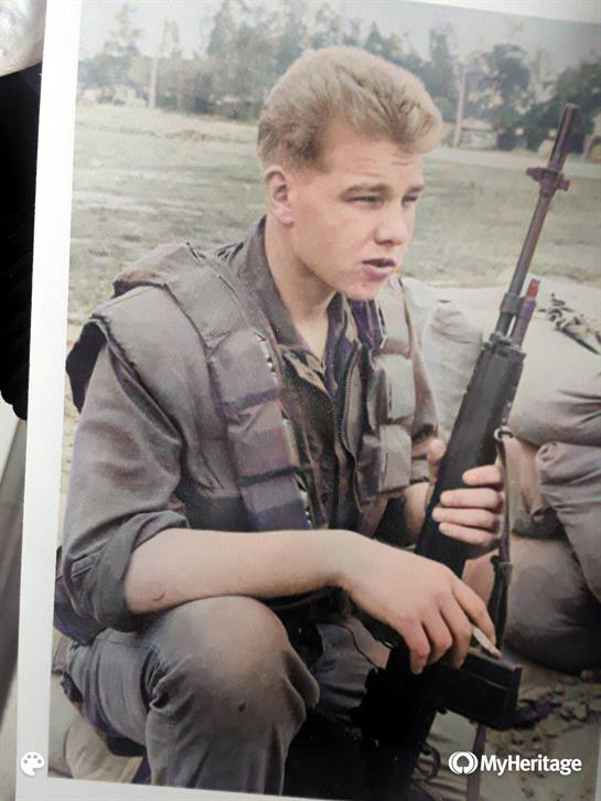 A young soldier sits on the ground holding a rifle, wearing military attire and focused on training.