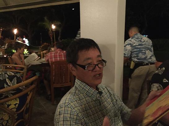 Group of friends enjoys a lively dinner at a tropical location under dim lighting.