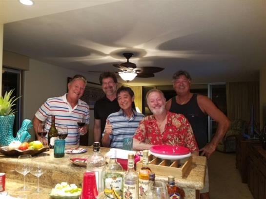 Five friends celebrate with drinks and food around a kitchen island in the evening.