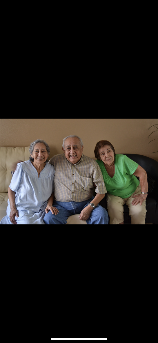 Three older adults sit together on a couch, sharing smiles and laughter in a warm atmosphere.